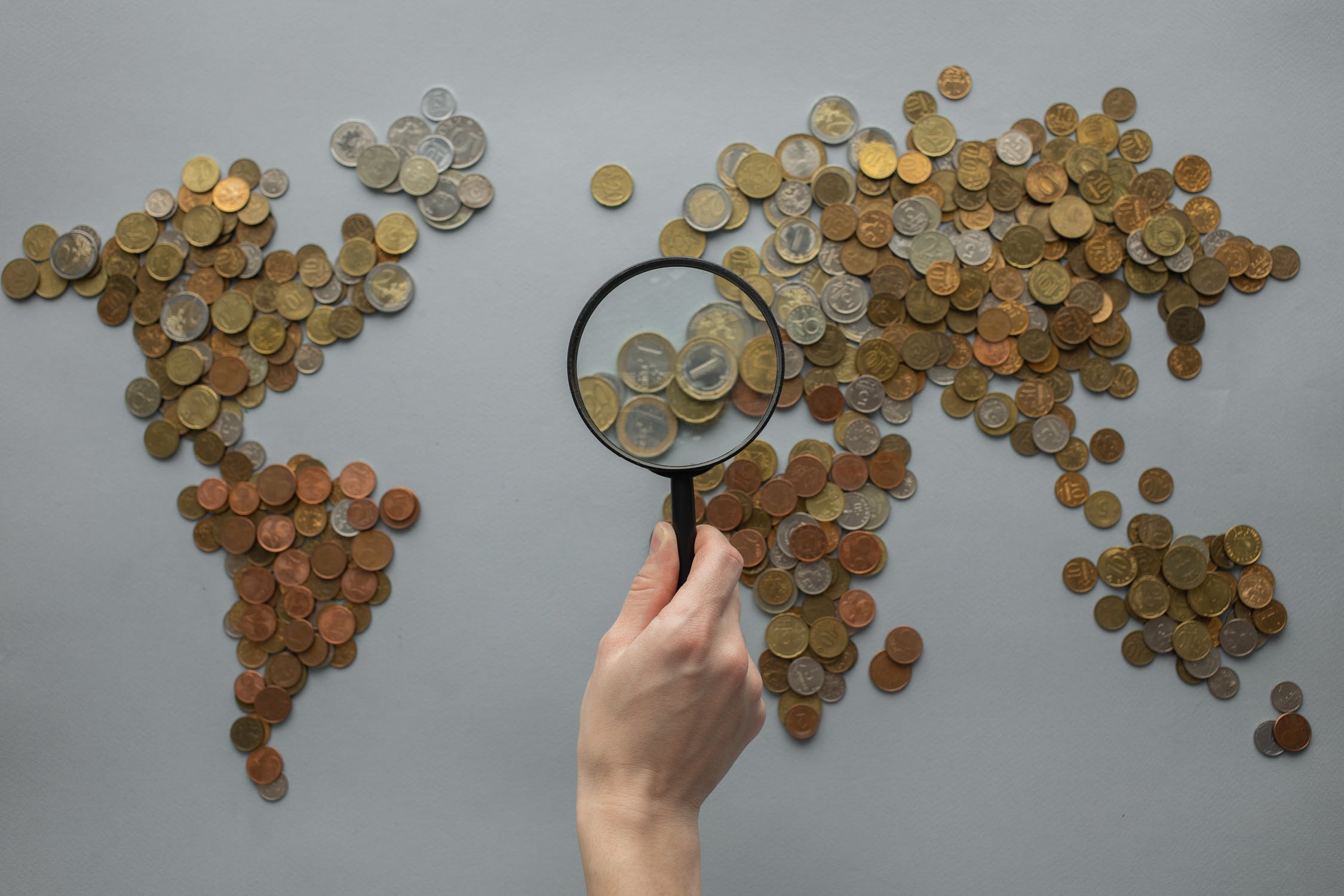 hand holding magnifying glass over map of the world made of coins