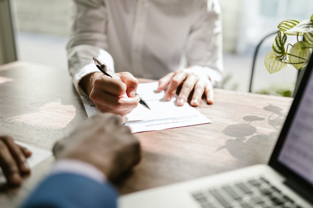 person filling out paperwork at table with second person