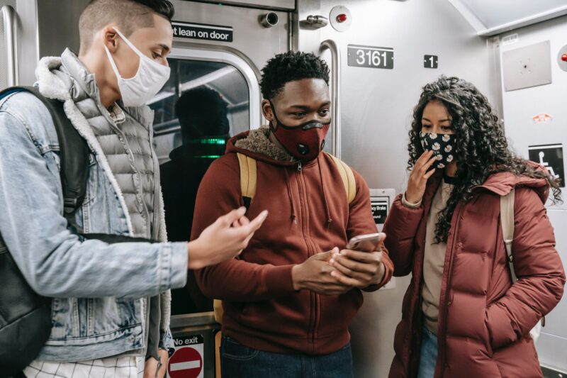 Faceless multiethnic students in masks in subway train with phone