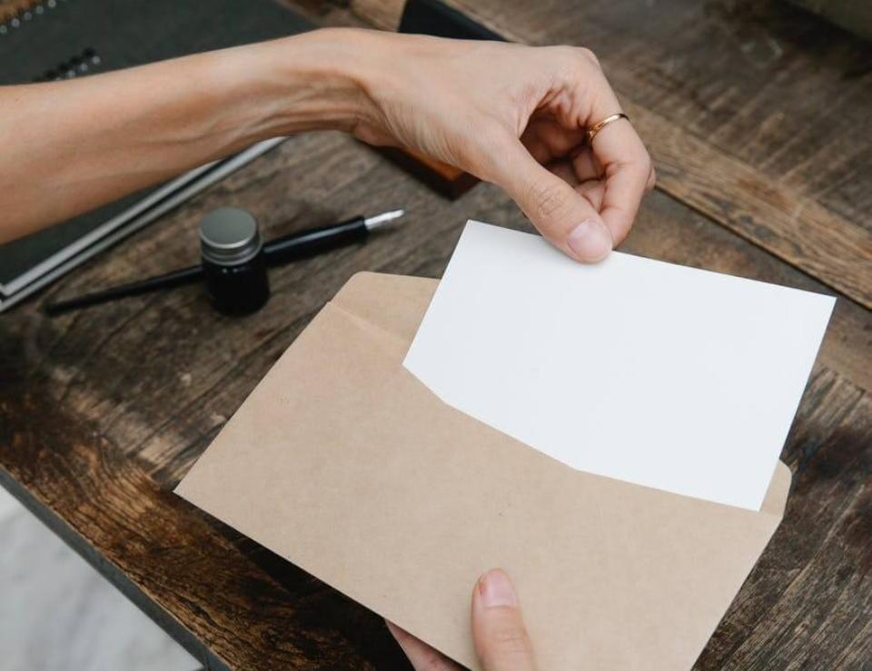 Crop unrecognizable woman placing blank paper in envelope