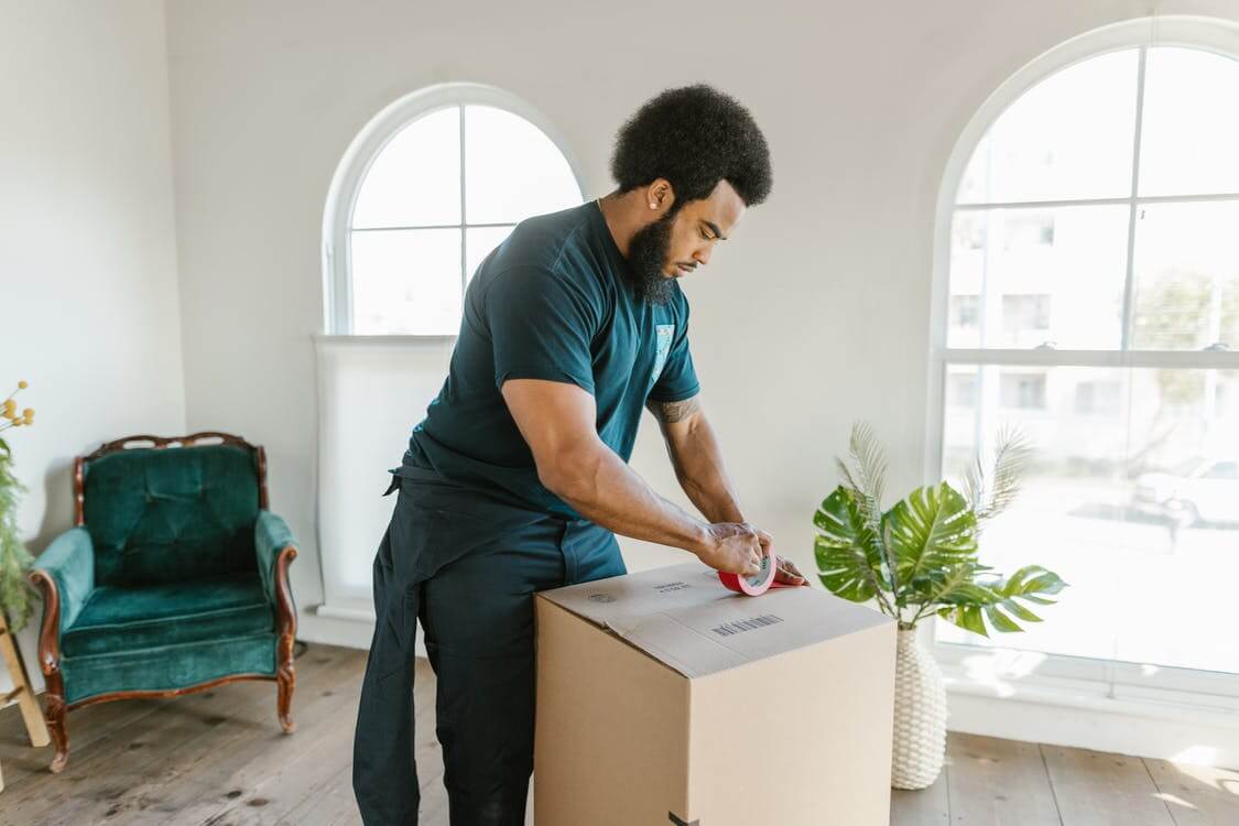 Man in Blue T-shirt and Blue Denim Jeans Holding White Box Man in Blue T-shirt and Blue Denim Jeans Holding White Box