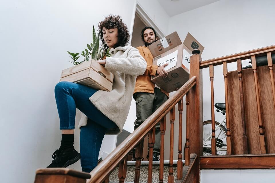 couple going down the stairs with box of books and plants