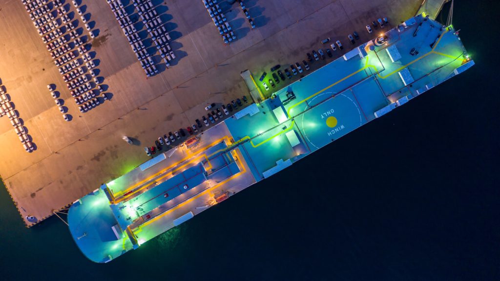 Aerial top view car carrier vessel at night, rows of new cars at night waiting to be dispatch and shipped import export new cars.