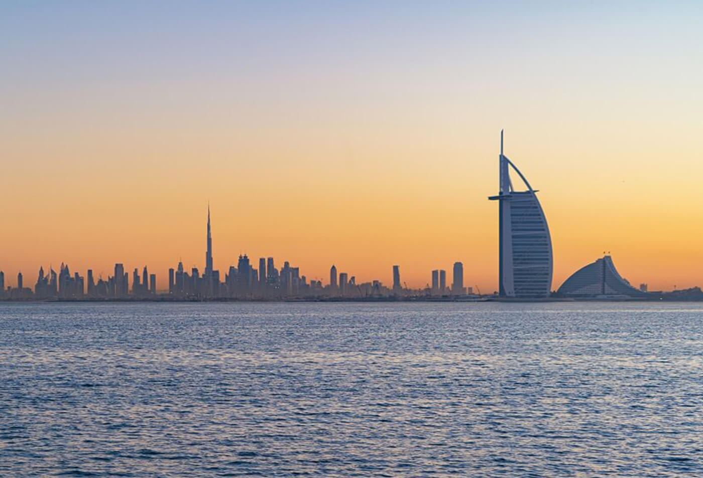 Burj Al Arab in Jumeirah Island or boat building with waves on sea beach, Dubai Downtown skyline, United Arab Emirates or UAE. Financial district in urban city. Skyscrapers at sunset.