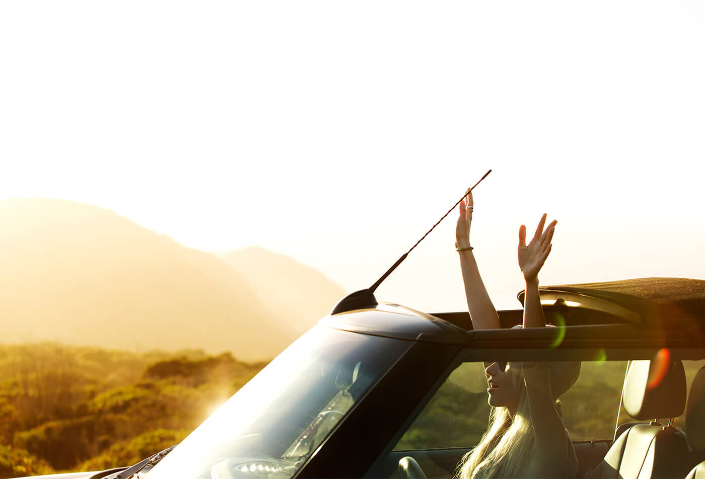 Woman raising arms through sun roof in car
