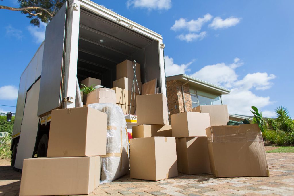 Cardboard boxes outside moving van and house in sunny driveway 1 Cardboard boxes outside moving van and house in sunny driveway