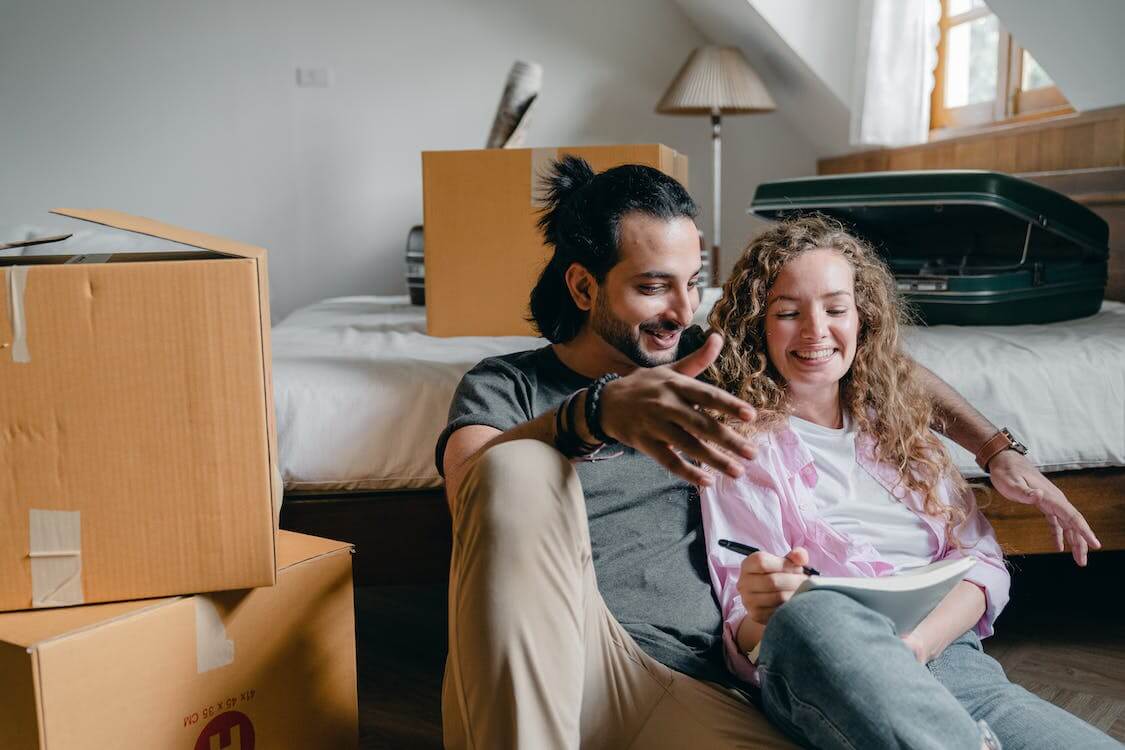couple taking notes, surrounded by moving boxes in new living space
